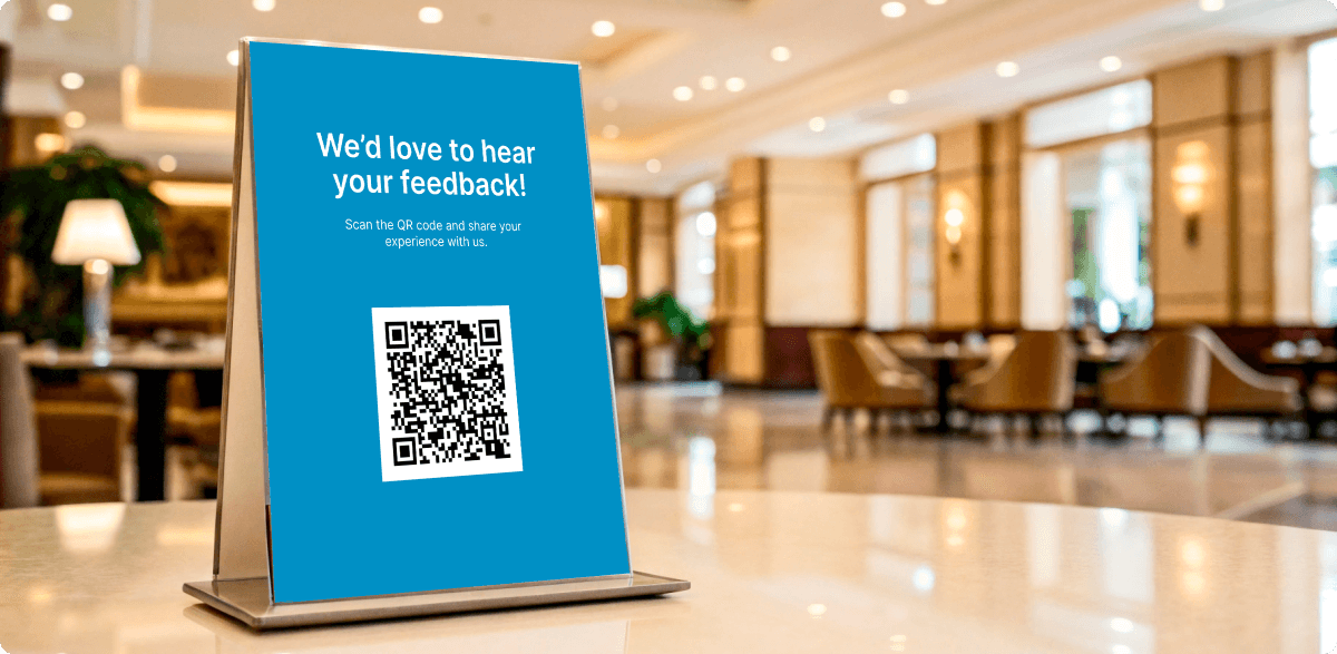 Blue table tent sign with QR code in a hotel lobby, asking guests for feedback.
