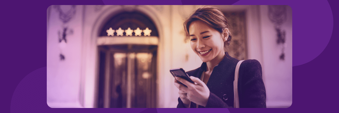 Smiling woman on phone in front of a hotel, showing 5-star rating, symbolizing positive reviews and mobile booking.